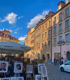 many pictures are on easels in front of buildings and people walking down the street