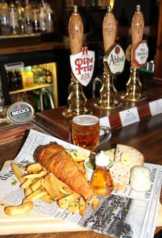 fish and chips with beer in the background on a bar top, next to two beers