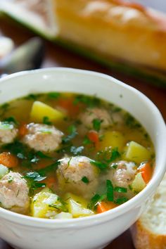 a bowl of soup with meatballs, carrots and celery next to bread