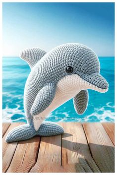 a stuffed dolphin sitting on top of a wooden floor next to the ocean with waves