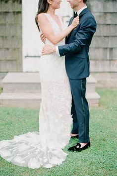 a bride and groom standing together in front of a building with grass on the ground