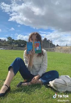 a woman sitting in the grass holding up a book to her face and reading it