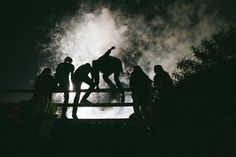 silhouettes of people standing on a fence with fireworks in the sky behind them at night