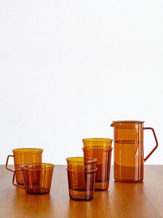 five brown glass cups sitting on top of a wooden table next to a pitcher and two glasses