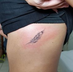 a woman's stomach with a small feather tattoo on it