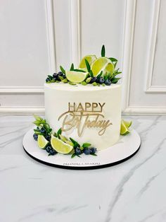 a white and gold happy birthday cake with lemons, blueberries and limes