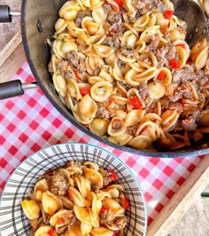 pasta with sausage and peppers in a skillet on a table next to a red checkered tablecloth