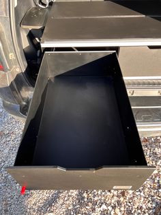 an open drawer in the back of a truck with gravel on the ground next to it