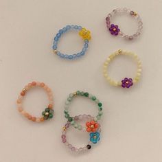 six bracelets with flowers and beads are arranged on a white surface, including one bead