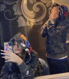 two people in front of a mirror with their cell phones up to their ears and one person taking a selfie