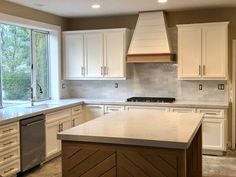 a kitchen with white cabinets and an island in the middle is shown, while a large window looks out onto trees