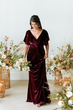 a woman standing in front of flowers wearing a burgundy velvet wrap dress with short sleeves