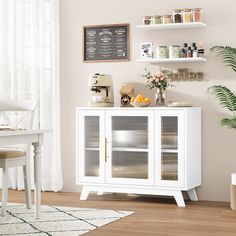 a white cabinet sitting in front of a window next to a potted plant on top of a wooden floor