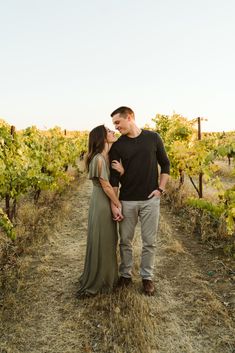 a man and woman standing next to each other on a dirt road surrounded by vines