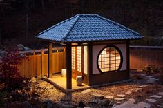 a small gazebo lit up at night in a garden with rocks and trees around it