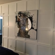 an abstract painting hangs on the wall next to a bed in a room with white paneling