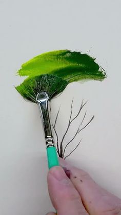 a person holding a paintbrush with green leaves on it's tip, and the brush is pointed to the side