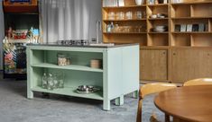 a kitchen with wooden shelves and green cabinetry in it's center area, next to a dining room table