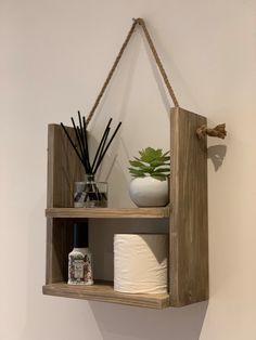 a wooden shelf with two shelves holding toilet paper and a potted succulent