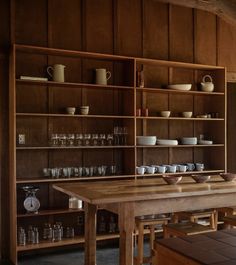 a wooden table topped with lots of bowls and cups next to shelves filled with glasses