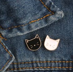 two cat pins sitting on top of a pair of blue denim jeans, one black and the other white