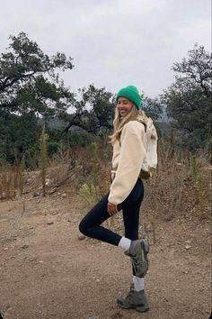 a woman standing in the middle of a dirt road with her legs crossed and smiling