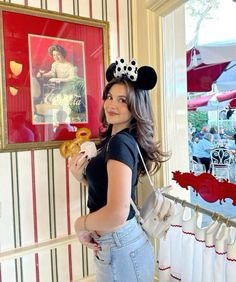 a woman holding a donut in her right hand and wearing a minnie mouse ears headband