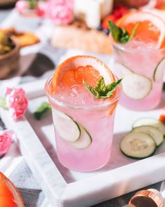 two glasses filled with cucumber, orange and mint cocktails on a tray