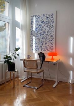 a cat sitting on top of a wooden desk next to a lamp and potted plant