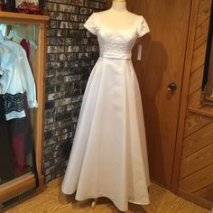 a white dress is on display in front of a brick wall and wooden flooring