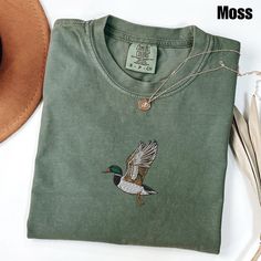 Embroidered Duck Comfort Colors Shirt | Animal Lover Shirt | Embroidery Shirt | Embroidered Gift | Duck Shirt Matching Sweatshirt: https://printworkshopcompany.etsy.com/listing/1767779984/embroidered-duck-sweatshirt-animal-lover ** VIP Email List Be sure to join our VIP Email list for new product releases, special promotions, and giveaways! https://email.everbee.io/subscribe?shopName=PrintWorkshopCompany ** HOW TO ORDER 1. Check our photos for sizing and color options. 2. Select your size and color from the drop-down menus. 3. Click "ADD TO CART" to add the shirt to your cart. 4. Click "PROCEED TO CHECKOUT" to purchase your shirt. ** DETAILS: The garment-dyed t-shirt by Comfort Colors is a customizable tee made entirely from 100% ring-spun cotton. ** SIZING : - Please refer to size chart o Green Cotton Tops With Machine Embroidery, Fall Embroidered Crew Neck Shirt, Embroidered Crew Neck Shirt For Fall, Embroidered Green Cotton Shirt, Green Embroidered Cotton Shirt, Cotton Tonal Embroidery Short Sleeve Tops, Cotton Tops With Tonal Embroidery And Short Sleeves, Duck Sweatshirt, Embroidered Duck