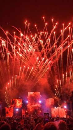 fireworks are lit up in the night sky as people watch from their seats at an outdoor concert