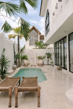 an outdoor swimming pool with lounge chairs and palm trees in the foreground, surrounded by white stucco walls