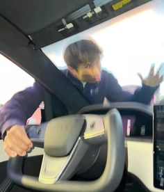 a man driving a car with his hand on the steering wheel and another person behind him