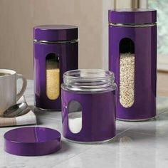 purple kitchen canisters with lids and spoons next to coffee cup on counter