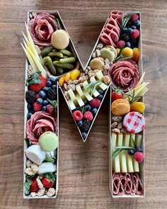 the letter m made out of food is displayed on a wooden table with fruit and veggies