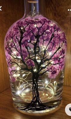 a glass bottle with a pink tree painted on the inside and lights in the outside