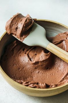 a wooden bowl filled with chocolate frosting and a spatula in the top half