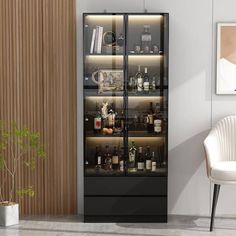 a glass door cabinet with bottles and glasses on it next to a white chair in a living room