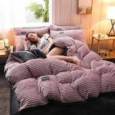 a woman laying on top of a bed covered in pink and white comforter next to a window