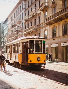 a yellow trolly car is on the street in front of some buildings and people