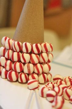 there are many red and white candies on the table next to a paper cone