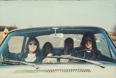 three women sitting in the front seat of a car with their hands on the steering wheel