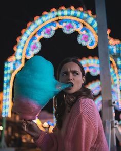 a woman holding an ice cream cone in front of a ferris wheel at night time