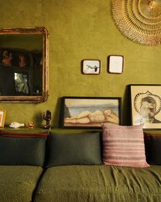 a living room with green walls and pictures on the wall next to a couch in front of a mirror