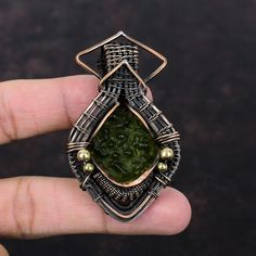 Note : Due to the natural formation of this gemstone. Slight variation in design and color are to be expected.  Moldavite Pendant Copper Wire Wrapped Pendant Moldavite Jewelry Unique Gemstone Pendant Gift For Mother Copper Wire Jewelry Handmade Pendant Handmade Copper Pendant SKU : VFWP-1714 Gemstone : Moldavite  Stone Shape : Round     Metal Purity : Copper Pendant Length : 71 MM   Pendant Width : 36 MM Handmade Green Fusion Gemstones, Handmade Green Tourmaline Gemstones, Wire Wrapped Jewelry Pendant, Moldavite Pendant, Moldavite Jewelry, Moldavite Stone, Wire Wrapped Bangles, Copper Wire Jewelry, Bijoux Fil Aluminium