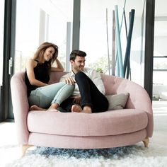 a man and woman sitting on a pink chair in front of a large window together