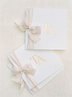 two folded cards with bows on them sitting next to each other, one is white and the other has gold foil