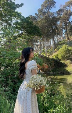 a woman in a white dress is standing by the water and holding a bouquet of flowers