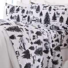 a bed covered in black and white sheets with trees printed on the sheet set, along with pillows